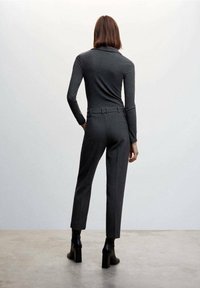 Strak aansluitende donkergrijze turtleneck met ribbelstructuur, gecombineerd met hooggetailleerde grijze broek en zwarte hakken met enkellaarzen.