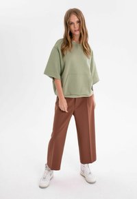 Överdimensionerad olivgrön sweatshirt med framficka, kombinerad med högmidjade bruna vida byxor och vita sneakers.