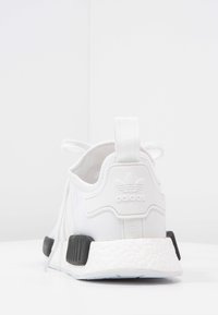 Vita Adidas NMD sneakers med en texturerad ovandel, svarta detaljer vid hälen och en tjock vit Boost-sula. Baksidan visar varumärket.