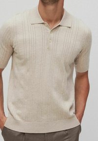Beige short-sleeve polo shirt with a textured knit, featuring vertical stripes and a three-button placket. Ribbed hem and collar.