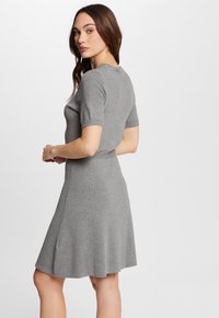 Grijze gebreide jurk met korte mouwen en een aansluitende top, die zachtjes uitloopt naar een knielange rok. Glad textuur, eenvoudig ontwerp, geen zichtbare patronen.