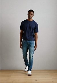 Camiseta de algodón azul marino combinada con jeans de denim azul claro y zapatillas blancas. Diseño sencillo con un corte relajado y detalles de costura visibles.