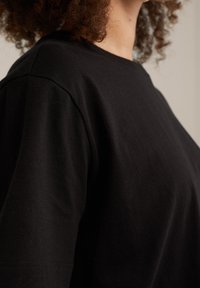 Černé bavlněné tričko s volným střihem, krátkými rukávy a hladkou texturou. Výstřih je zaoblený a jednoduchý.