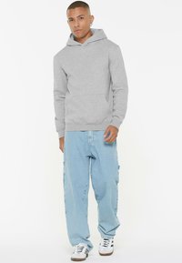 Gray hooded sweatshirt with a front pocket, worn with light blue loose-fitting jeans and white sneakers. Smooth texture, casual design.