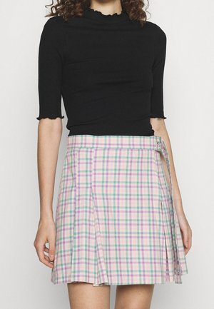 Vrouw die een zwart aansluitend topje draagt met geschulpte randen en een geplooide pastelkleurige geruite rok met een gesp aan de zijkant.