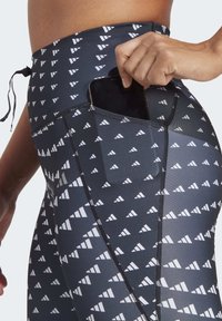 Zwart-witte leggings met een patroon en een zijzak. Het ontwerp bevat driehoekige vormen op een gladde, rekbare stof.