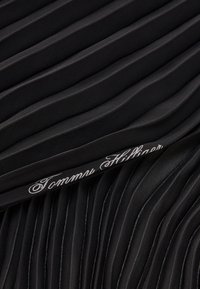 Tissu plissé noir avec une texture douce, ornée d'un logo "Tommy Hilfiger" brodé en blanc le long du bord inférieur.