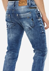 Denim jeans met een vervaagde blauwe afwerking, vijf zakken en een leren label in bruin. Beschikt over een ritszak en gestructureerde delen nabij de zakken.