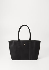 Bolso tote negro hecho de un material suave, con dos asas resistentes, un logo dorado y una marca sutil en los lados.