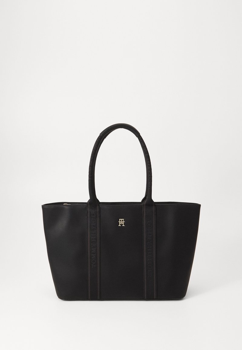 Bolso tote negro hecho de un material suave, con dos asas resistentes, un logo dorado y una marca sutil en los lados.