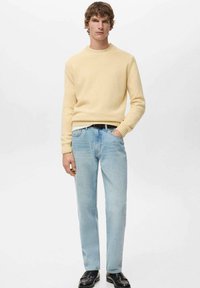 Jasnożółty sweter z dzianiny z żebrowanymi mankietami, w połączeniu z jasnoniebieskimi prostymi dżinsami. Czarny pasek i błyszczące czarne buty dopełniają strój.