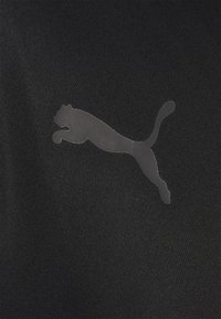 Svart tyg med en slät struktur som har en genomskinlig, hoppande puma-logotyp i mitten. Enkelt, odekorerat design.