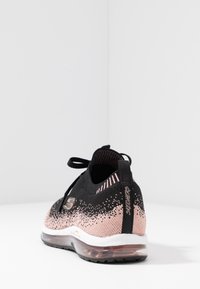 Svart och ljusrosa träningssko med en stickad ovandel, texturerade detaljer och en transparent luftkuddesula. Har dragremsa och logotyp.