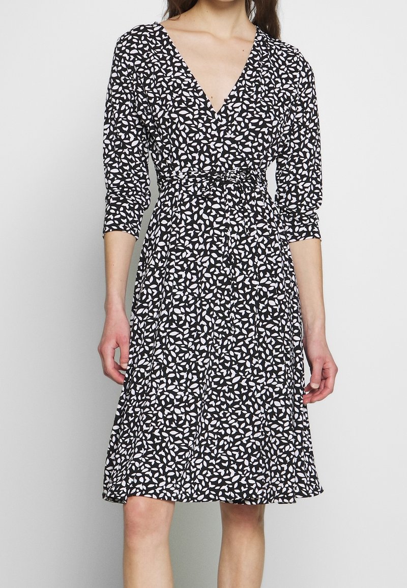 Czarna sukienka z białym wzorem liści, dekolt w kształcie litery V, rękawy o długości trzech ćwierci, dopasowana w talii i zwiewny dół. Lekki materiał o miękkiej teksturze.