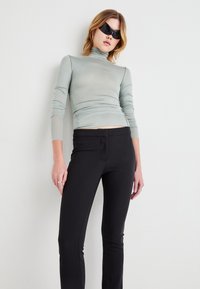 Lys grønn, langermet turtleneck med rynkete sider, kombinert med høyt liv sorte bukser. Modellen har på seg svarte solbriller.