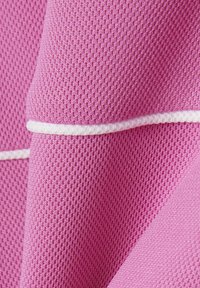 Primer plano de tela rosa texturizada con una costura blanca elevada que corre horizontalmente a lo largo del material.