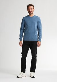Pulover tricotat albastru cu decolteu în V, cu mâneci lungi, asortat cu blugi negri slim-fit și adidași albi. Textură netedă, croi lejer.