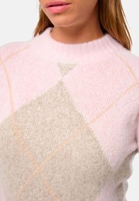 Pull léger rose avec un col côtelé. Présente un motif de losanges beige avec des coutures orange. Texture douce, tissu de poids moyen.