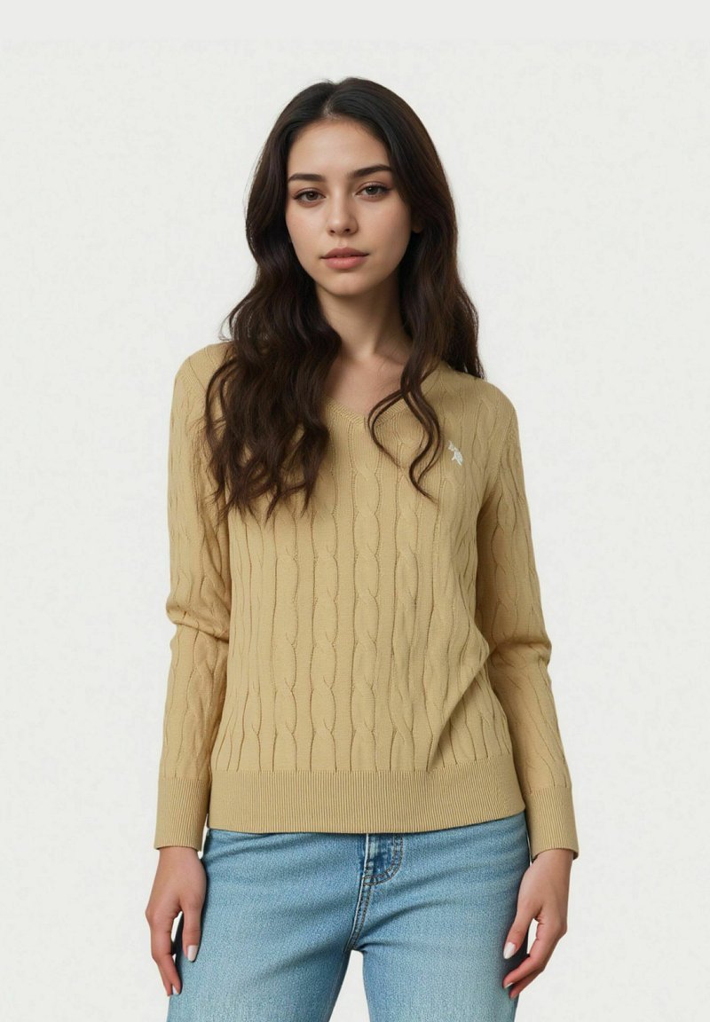 Pulover tricotat cu model în relief, de culoare galben deschis, cu mâneci lungi și manșete canaletate, având un mic emblemă albă pe piept. Asortat cu blugi albaștri.