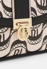 Zwarte en beige handtas met een gladde textuur, voorzien van een golfpatroon en een gouden ronde logo-sluiting.