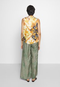 Multifarvet blomsterærmeløs top i gul, orange og marineblå, parret med grønne mønstrede wide-leg bukser. Glat stof med varierede designs.