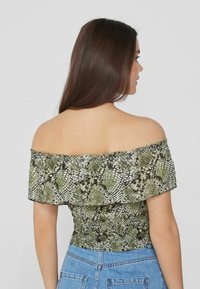 Top off-the-shoulder in stampa serpente verde, con vita arricciata e volant. Tessuto leggero con una texture liscia.
