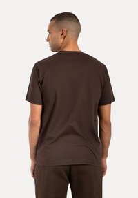 Brązowa bawełniana koszulka z okrągłym dekoltem, krótkimi rękawami i luźnym krojem. Posiada minimalne szwy i gładką teksturę.