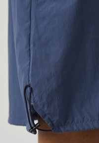 Modré, lehké šortky s texturovanou tkaninou, bočními švy a stahovací šňůrkou na lemu pro přizpůsobení.