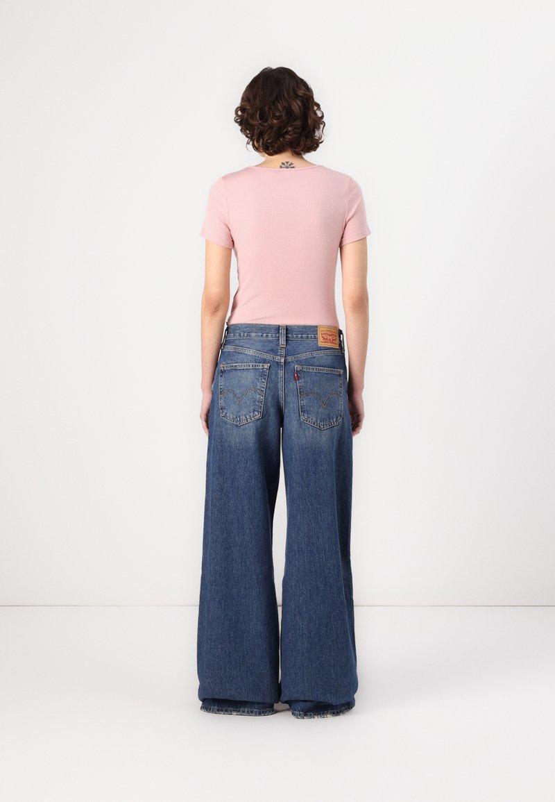 Lichtroze aansluitend T-shirt gecombineerd met wijde blauwe denim jeans, voorzien van een leren label aan de achterkant en twee achterzakken.