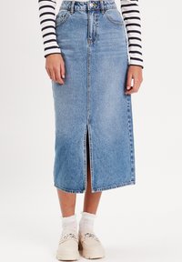 Jupe en denim bleu clair, longueur genou avec une fente à l'avant. Équipée de passants de ceinture et d'un design à cinq poches, assortie de chaussettes blanches et de chaussures claires.