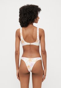 Pasztell színű virágmintás bikini, széles pántos, alacsony hátú toppal, amelyet egy hozzáillő, magas derekú alsó egészít ki.