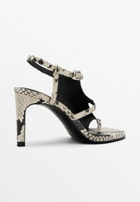 Högklackad sandal med ett ormskinnsmönster, i svart och beige färger, med en smal klack, tunna remmar och en spänne för stängning.