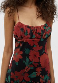 Robe florale avec une base noire, motifs de fleurs rouges et vertes, corsage froncé et fines bretelles. Texture de tissu lisse.