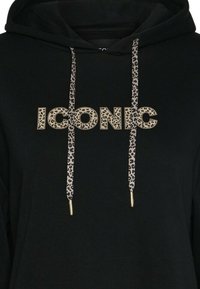 Sudadera negra con detalles de estampado de leopardo. Presenta la palabra "ICONIC" en letras doradas y en negrita. Los cordones tienen patrones de leopardo con puntas doradas.
