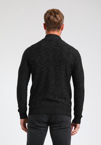 Czarny sweter w paski z prążkowanym kołnierzem i mankietami. Teksturowana tkanina o dopasowanym kroju, widoczna od tyłu na neutralnym tle.