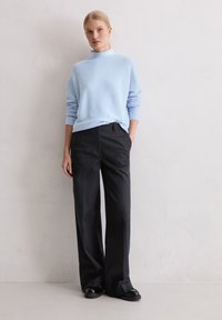 Maglione azzurro chiaro con colletto alto, abbinato a pantaloni larghi scuri. Tessuto morbido e design su misura. Scarpe nere completano l'outfit.