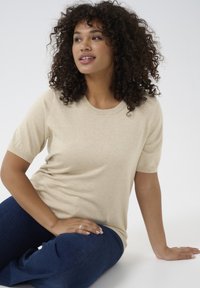 Beige short-sleeve sweater made of soft material, featuring a round neckline and a relaxed fit, paired with dark blue jeans.