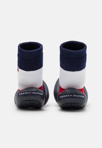 Námořnické, bílé a červené tenisky ve stylu ponožek s měkkým pleteným svrškem a černou gumovou podrážkou. Logo "TOMMY HILFIGER" na patě.