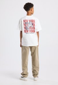 Valkoinen ylipitkä t-paita, jossa on punaiset "NEW YORK" -tekstit sekä sarjakuvahahmo, joka pelaa koripalloa. Yhdistä beigenväristen housujen ja valkoisten sneaker-kengät kanssa.