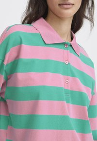 Pruhovaná polo košile v růžové a zelené barvě, vybavená límečkem, třemi knoflíky a jemnou texturou. Design zahrnuje široké, rovnoměrné pruhy.