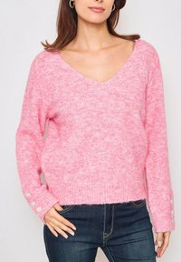 Pull en tricot texturé rose avec un col en V, des épaules tombantes et des accents de boutons sur les poignets. Coupe décontractée et ourlet côtelé.
