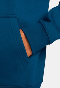 Teal sweatshirt med en ficka framtill. Har ribbade ärmslut och nederkant. Slät textur och sömnadsdetaljer syns.