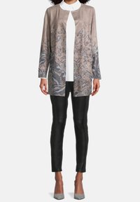 Chaqueta de flores en color beige claro, con mangas largas, apertura frontal y dos bolsillos, combinada con pantalones negros ajustados y tacones grises.