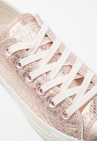 Baskets basses Converse avec dessus texturé métallisé or rose et lacets blancs sur une semelle blanche.