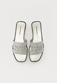 Chanclas grises con letras recortadas "KARL", acabado de purpurina metálica y suela negra. Diseño liso y plano con puntera abierta.