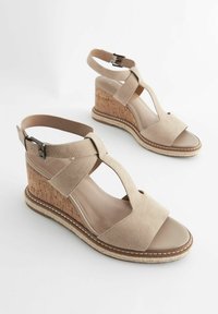 Beige wedge sandály s korkovým podpatkem, svrchní část z semiše a nastavitelným řemínkem kolem kotníku. Vybaveny výřezovým designem na přední straně.