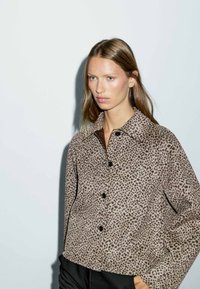 Giacca button-up in stampa leopardata nei toni marroni e beige, con colletto, bottoni neri e un design cropped in un tessuto testurizzato.
