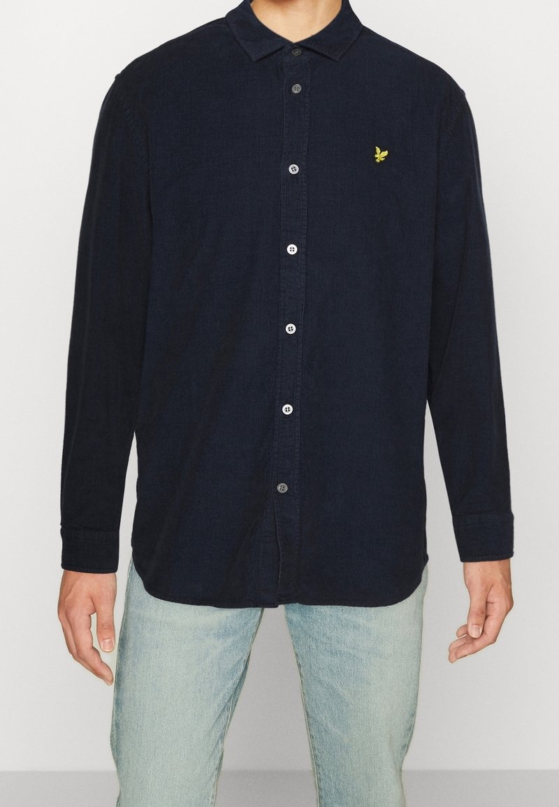 Granatowa koszula zapinana na guziki, wykonana z fakturowanej tkaniny, z kołnierzykiem, długimi rękawami i małym żółtym logo na piersi.