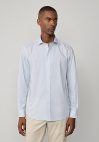 Lichtblauw overhemd met knopen, met een geruit patroon, lange mouwen en een kraag. Gemaakt van een gladde stof, met witte knopen.