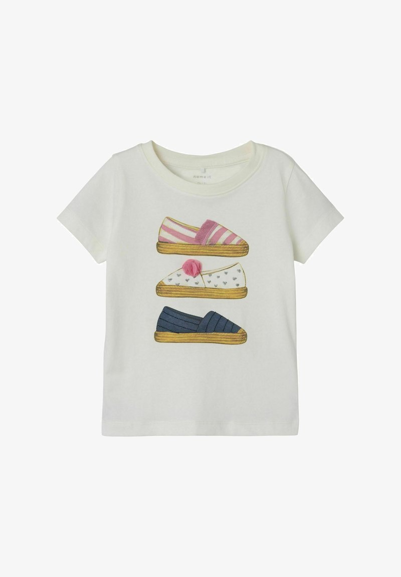 Hvid t-shirt med illustrerede sko: lyserød stribet slippers, hvid slippers med hjerter og blå slippers med striber. Blødt bomuldsstof.